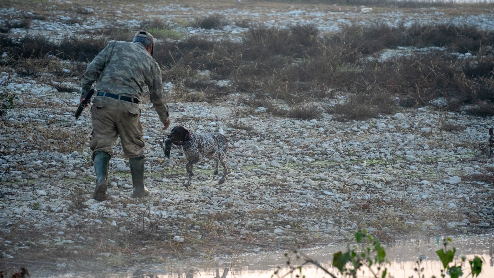 A hunter and his dog on rocky outdoor terrain
